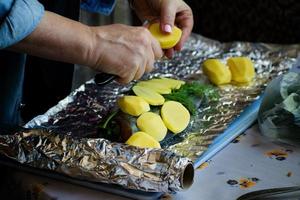 la mujer está cocinando salmón con patatas y eneldo en papel de aluminio. foto