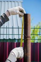 A man measures metal pipes with a tape measure. Construction of the fence. photo