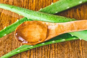 Close up of Aloe vera gel on wooden spoon with aloe vera on wooden table. photo