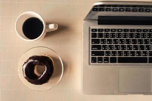 Top view of laptop with coffee cup and donut on table. photo