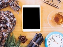 Top view of tablet with tea cup,clock, scarf and christmas decoration on wooden table. photo