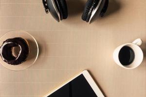 Top view of headphones with tablet, coffee cup and donut on table. Free space for text photo