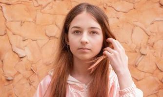 retrato de niña adolescente en la pared beige. la niña arregla su cabello. foto