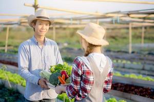 hermosa mujer y hombre asiáticos que sostienen verduras orgánicas frescas con canasta juntos en la granja hidropónica, cosecha y agricultura y cultivo para alimentos saludables y concepto de negocios. foto