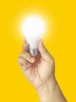 Human hand holding light bulb illuminated on yellow background. Creativity, inspiration, flat lay design idea photo