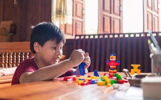 el niño asiático se está volviendo creativo al ensamblar coloridos ladrillos de plástico en robots y aviones en una mesa de madera feliz y divertido en casa. concepto de creadores de niños. foto