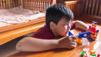 Asian boy is getting creative with assembling colorful plastic bricks into robots and planes on a wooden table happy and fun at home.Kid Creators concept. photo