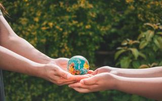 Close-up of a woman's hand giving an asteroid world to a boy on a blurry green background.hands holding planet earth save the earth. photo