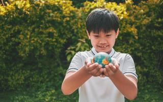 Planet earth in the boy's hands saves and protects the world over blurred green nature background. Environmental concept on Earth Day. photo