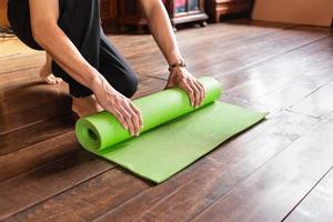 primer plano de un hombre que hace rodar a mano una alfombra de yoga verde o una alfombra de ejercicio después de hacer ejercicio de yoga matutino en casa. vida sana y concepto de vida saludable. foto