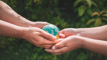 Close-up of a woman's hand giving an asteroid world to a boy on a blurry green background.hands holding planet earth save the earth. photo