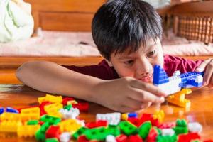 Asian boy is getting creative with assembling colorful plastic bricks into robots and planes on a wooden table happy and fun at home.Kid Creators concept. photo