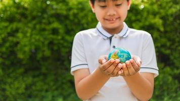 Planet earth in the boy's hands saves and protects the world over blurred green nature background. Environmental concept on Earth Day. photo