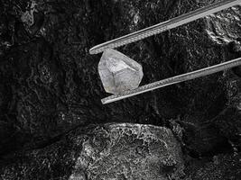 Natural diamond held in tweezers on black coal background photo