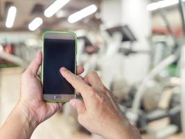 hand holding mobile smart phone with blur fitness gym equipment background photo