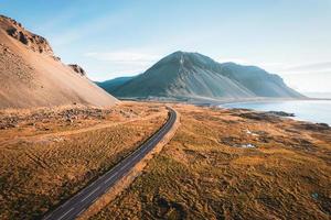 Scenic asphalt road with mountain and golden field on coastline in summer at Iceland photo
