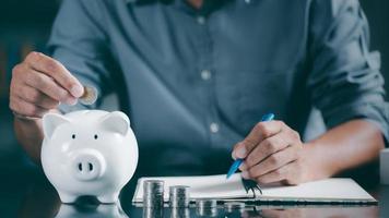 A young man puts coins in a piggy bank to save and record his growth in accounting, finance and investment ideas for planning and managing his retirement savings. photo