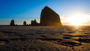 una puesta de sol dorada detrás de la hermosa roca pajar en cannon beach, oregon. foto