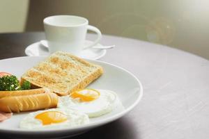 desayuno americano y café caliente en una taza de café de cerámica blanca sobre una mesa de madera con cálido sol matutino y fondo de lente. foto