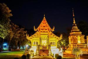 vista nocturna del santuario y la pagoda dorada en wat phra singh woramahaviharn, chiang mai, tailandia. foto