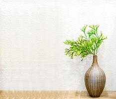Green plant in decorative brown vase put on wooden floor and front of white square pattern tile in the toilet. photo