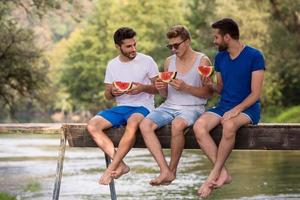 men enjoying watermelon while sitting on the wooden bridge photo