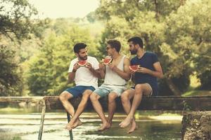 men enjoying watermelon while sitting on the wooden bridge photo