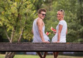 pareja disfrutando de la sandía mientras se sienta en el puente de madera foto