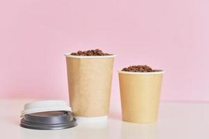 Two paper coffee cups with coffee beans on pink background photo