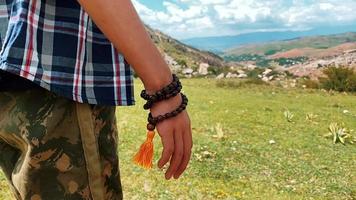 un tipo se para en una piedra sosteniendo un rosario musulmán en sus manos contra el fondo de las montañas video