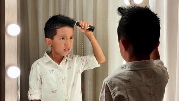 kleiner asiatischer junge, der sein haar vor einem spiegel macht