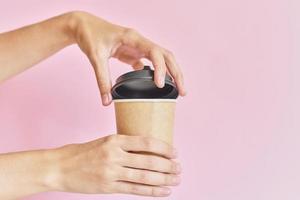 vaso de papel abierto de mano femenina con café sobre fondo rosa foto