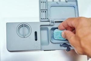 Hand putting soap tablet in the dishwasher machine photo