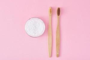 Two wooden bamboo toothbrushes and baking soda powder on a pink background photo