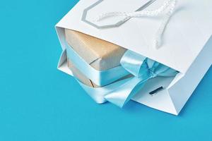 White shopping bag with gift box on blue background, top view photo