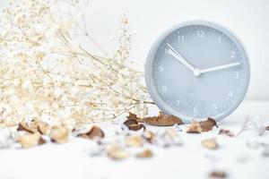 Classic alarm clock, flower branch and petals on a white table. photo