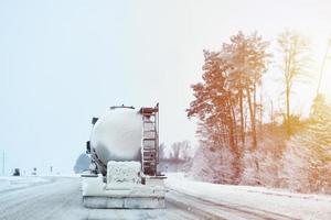 camión con tanque de carga en la carretera de invierno con nieve resbaladiza fuera de la ciudad, vista trasera foto