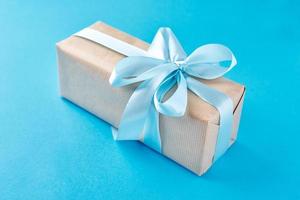 close up gift box in craft paper with blue ribbon on a blue background photo
