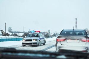 coche de policía con luces intermitentes rojas y azules detuvo el coche en la carretera nevada de invierno foto