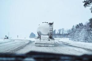 Truck with cargo tank on slippery snow winter road outside the city, back view photo