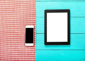 Electronic devices with place for text and red plaid tablecloth on blue wooden background. Top view and copy space. photo