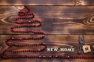 Christmas tree on wooden background with key to the house and keychain with inscription in English new home. Building or buying a house in New year. Mortgage, real estate rental. copy space, flatly photo