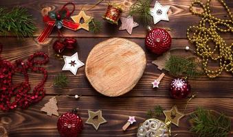 Christmas flat lay of red balloons and wooden stars and clothespins on a dark background with tree trunk section for notes in center. New year's frame, space for text. Xmas toys, beads, pine branches photo