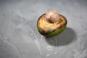 Spoiled avocado with green mold and black spots of rot and fungus on a gray background. Cut natural fruit, half with a round bone. Space for text photo