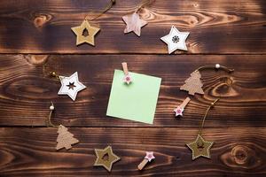 Christmas flat lay of wooden stars, fir trees and clothespins on a dark background with a square sheet for notes in the center. New year's frame, space for text. Xmas toys, to do list, a postcard photo