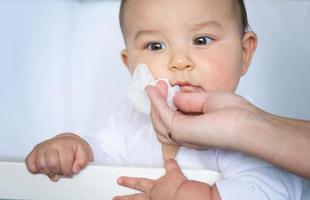 Mom wipes the baby's drool with a napkin. Baby care, teething, drooling. photo