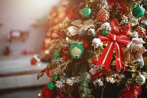 Christmas decor artificial Christmas tree close-up. Red and green toys, ribbons, glass owl, snow. Lights of garlands in the box. New year background photo