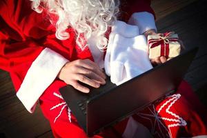 santa claus con una computadora portátil y un regalo en la mano. pedir regalos para navidad y año nuevo a través de la tienda en línea. contratar los servicios de un animador para las vacaciones. foto