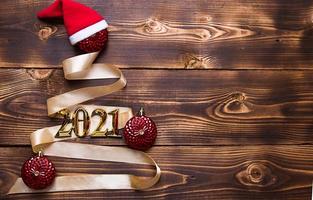 A Christmas tree made of gold ribbon with the numbers 2021 is decorated with red balloons on a dark wooden background. Flat lay. Space for text. New year, Santa hat. photo