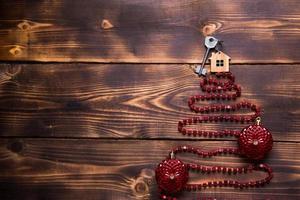 Key to the house with a keychain on top of Christmas tree made of red square beads. Flat lay on wooden background. Building or buying a house in new year. Mortgage, real estate rental. Space for text photo